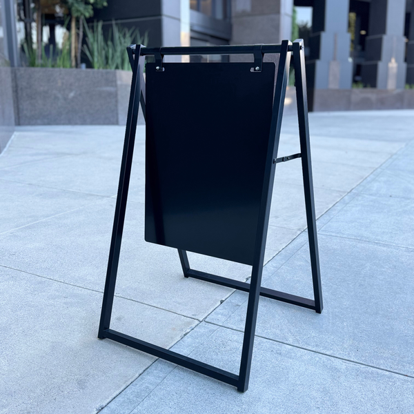 Black a-frame sign on a sidewalk with a building in the background