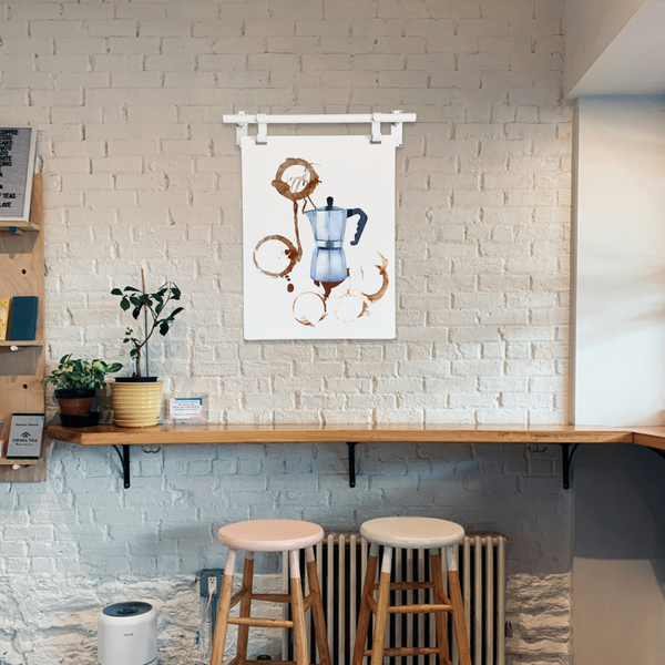 Coffee-themed wall art above a bar with stools in a cafe setting.