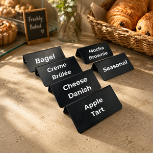 Black counter signs with dessert names on a table with baked goods in the background