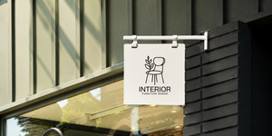 White blade sign with 'INTERIOR FURNITURE DESIGN' and a chair illustration hanging on a building.