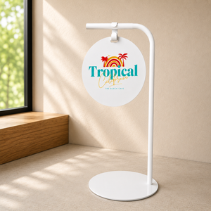 White round sidewalk sign featuring 'Tropical California' logo in a room with a window.