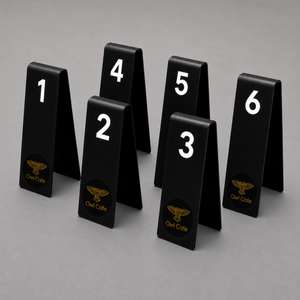 Six black A-frame table numbers 1 through 6 with white numerals and a gold Owl Cafe logo
