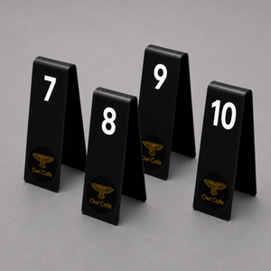Four black triangular table number signs displaying 7, 8, 9, and 10 in white, with gold Owl Cafe logos