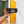 A black rectangular blade sign with yellow arrows and the words 'ORDER HERE' in white, held by a person's hands in front of a bright yellow door in an indoor room.