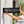 A black projecting metal custom sign for 'larana Spa salon' with a white leaf logo, being held against a light gray concrete wall by a person's hands and arms.