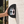 A black half round toilet blade sign mounted on a beige stone wall. The sign features the word 'TOILET' above male and female restroom icons on light blue and light pink backgrounds.