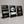 Three large black metal table countertop signs displayed on a gray surface against a gray background. The left sign says 'PLACE YOUR ORDER Here' with a yellow bell icon, the middle sign displays 'Wi Fi' card graphic, and the right sign says 'SCAN TO VIEW MENU' with a QR code and fork and knife icons.