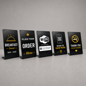 Five black metal large tabletop sign with yellow and white food-and-drink tableware graphics, shown on a gray surface against a gray background. The signs read Breakfast Served 6AM-10AM, Place Your Order Here, Wi-Fi Hotel, Scan to View Menu, and Thank You for Not Smoking.