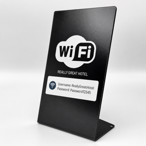 A black freestanding large metal counter sign with a white Wi-Fi logo and sample credentials, photographed on a clean light gray studio background.