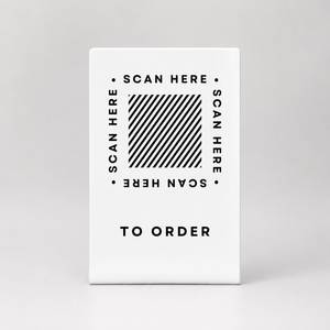 A white rectangular metal qr code sign with the words 'SCAN HERE' repeated around the square, and 'TO ORDER' printed below.