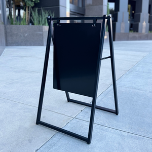 Black a-frame sign on a sidewalk with a building in the background