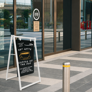 Outdoor sidewalk signboard advertising coffee and oat latte outside a building with glass doors.