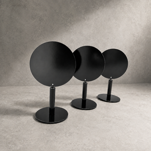 Three modern black tabletop counter sign with circular plates on slim stands, arranged in a row against a textured gray studio background.