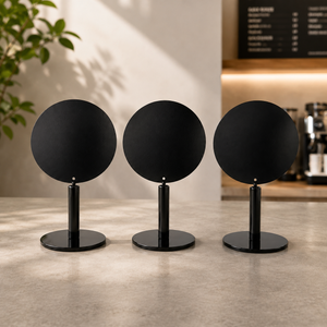 Three minimalist black round tabletop stands, arranged side by side on a light stone countertop in a softly lit interior setting.
