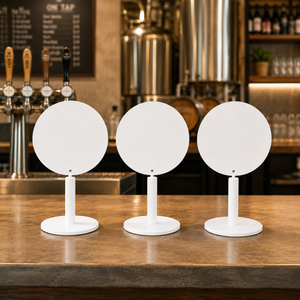 Three white modern round tabletop signs arranged side by side on a wooden bar counter. 
