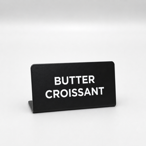Black cafe sign with 'BUTTER CROISSANT' text on a white background