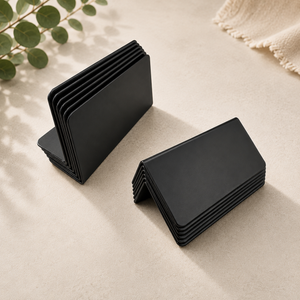 Stacks of black counter signs cards on a beige surface with a plant in the corner.