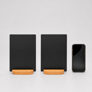 Two black rectangular display stands with light wood bases are shown on a light gray studio background, alongside a black smartphone for scale.