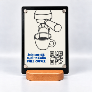 A vertical counter sign with 4 magnets showing a Coffee Club poster, illustrated espresso machine pouring into a cup, blue text reading 'JOIN COFFEE CLUB TO EARN FREE COFFEE,' a QR code, and a small wooden stand on a white studio background.